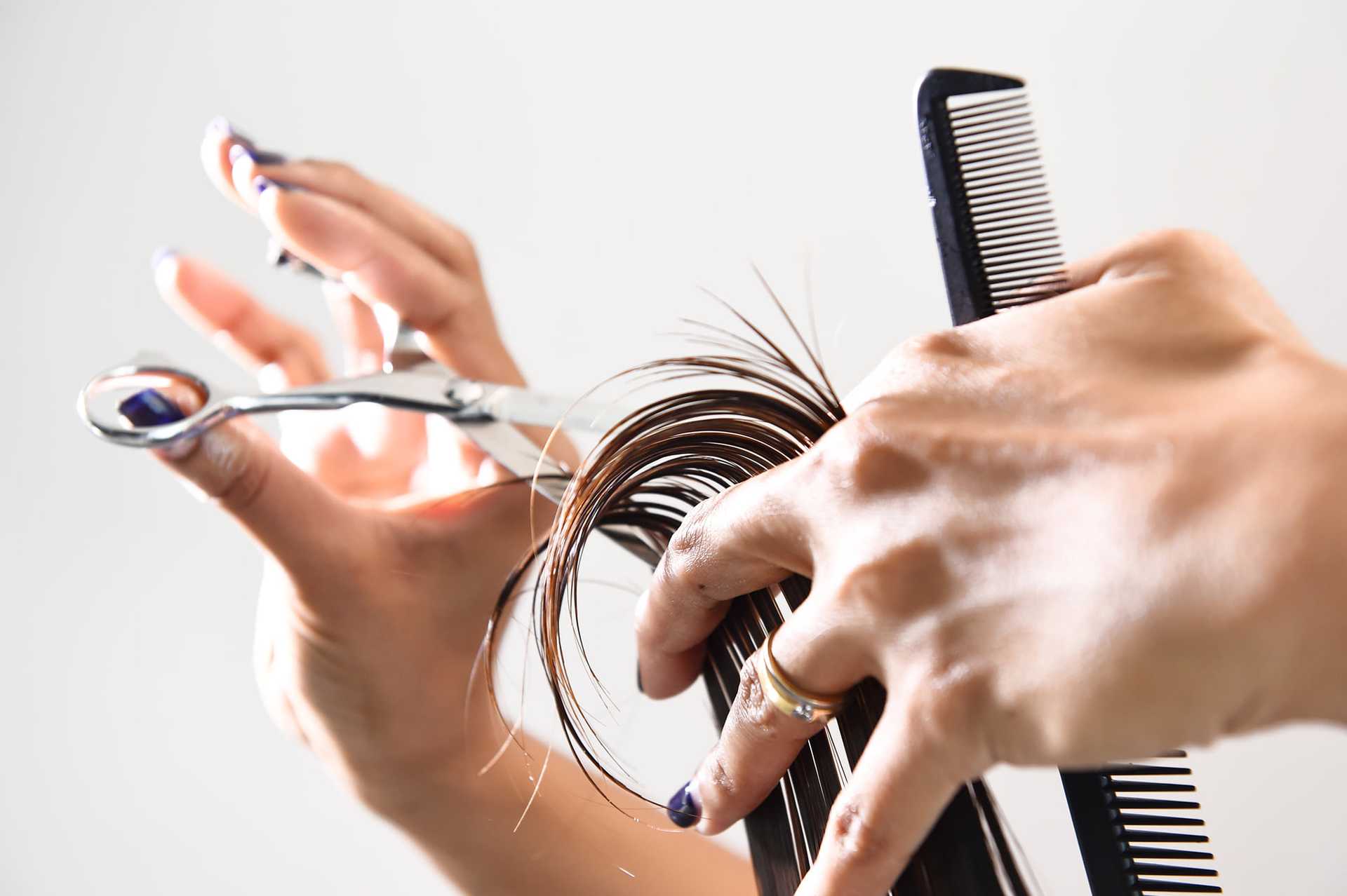 Haircutting close-up: hands trimming dark hair with scissors and comb.