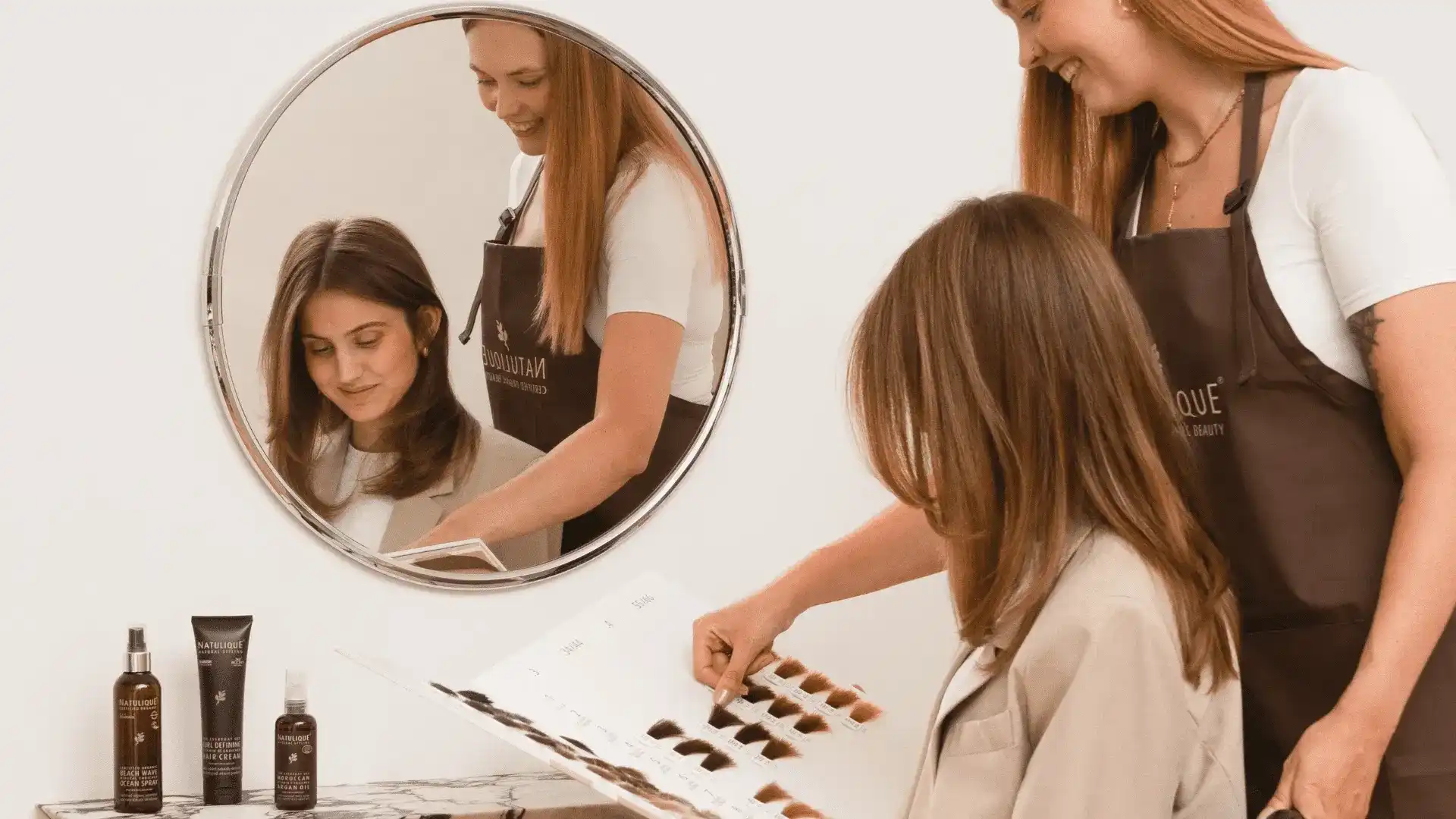 Hair stylist showing client color options in salon through mirror reflection.